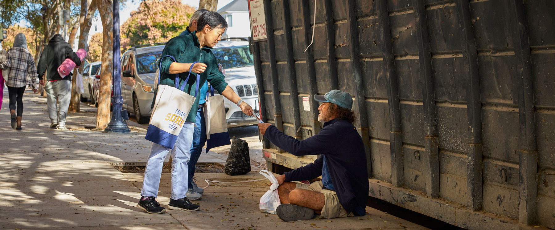 Outreach volunteer with man sitting on a sidewalk