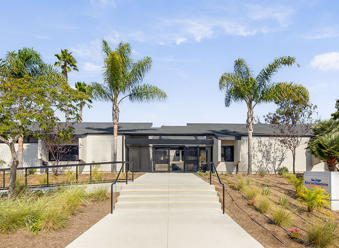 San Diego Rescue Mission homeless shelter building with palm trees and a walkway in Oceanside.