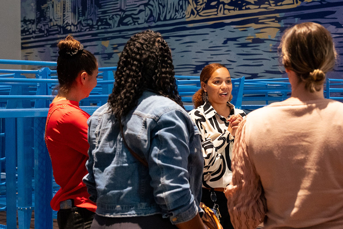 People touring a men's dorm room with blue beds and a San Diego mural at a homeless shelter in National City