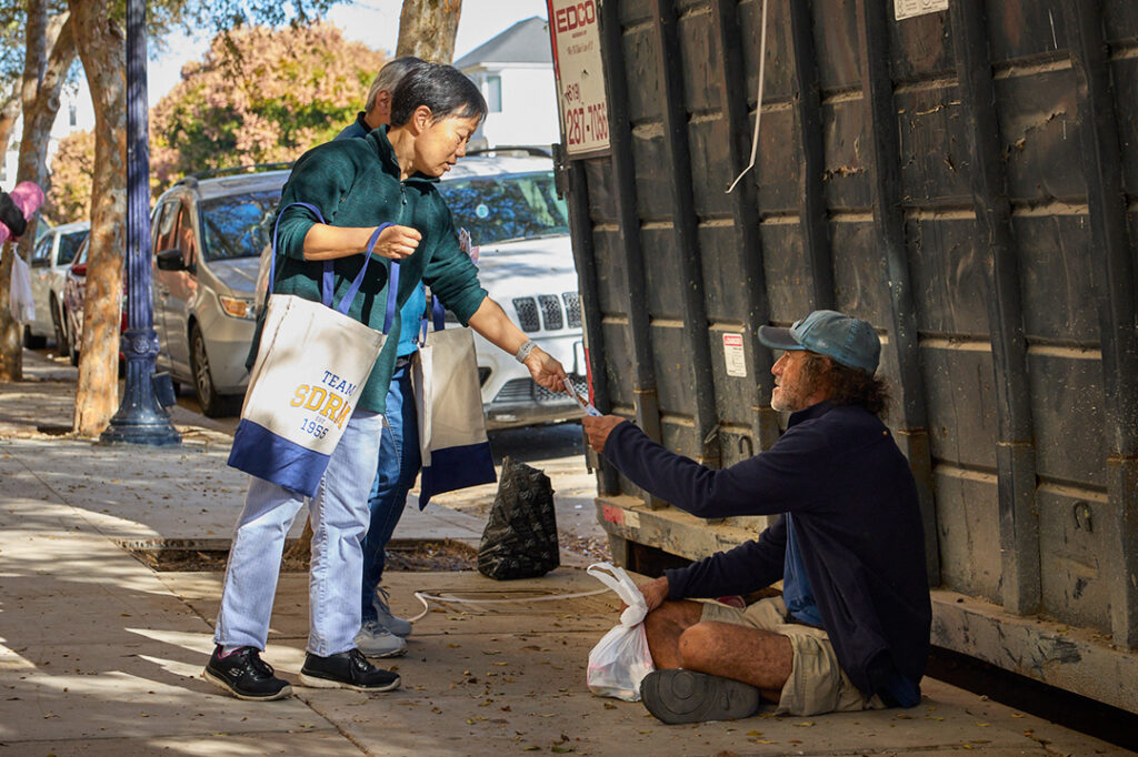 Outreach volunteer with man sitting on a sidewalk
